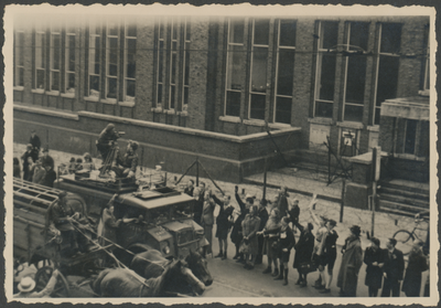 879278 Afbeelding van een geallieerd legervoertuig met op het dak een filmende cameraman voor het met versperringen ...